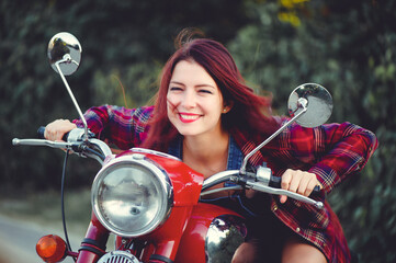 Plakat The biker is a beautiful cheerful girl sitting on her motorcycle, a little crazy. Wear short shorts. holding the steering wheel the wind blows the hair. Looks into the distance at the road