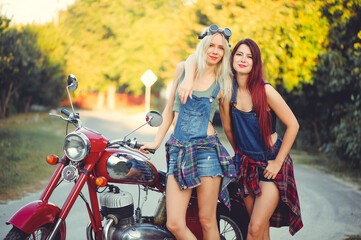Obraz na płótnie Canvas Young beautiful women ride a retro motorcycle. A talented girl in a blue overalls. They are standing near a motorcycle, funny go to the road. sale of spare parts. Place for text