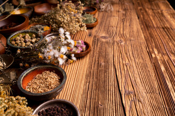 Fototapeta na wymiar Natural medicine background. Assorted dry herbs in bowls and brass mortar on rustic wooden table.