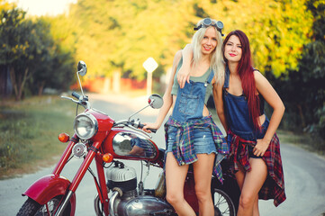 Fototapeta na wymiar Young beautiful women ride a retro motorcycle. A talented girl in a blue overalls. They are standing near a motorcycle, funny go to the road. sale of spare parts. Place for text
