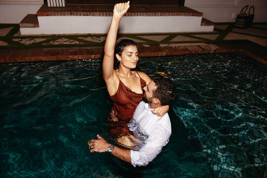 Young couple having fun in a swimming pool at night
