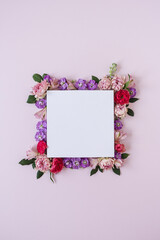 Frame made of rose flower buds on pink background and blank paper card sheet. Flat lay, top view. Copy space mockup.
