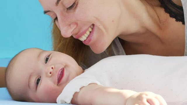 Tender loving mother kissing bonding with cute small baby girl daughter lying on bed. Happy caring mum and funny adorable infant child son playing having fun in bedroom.