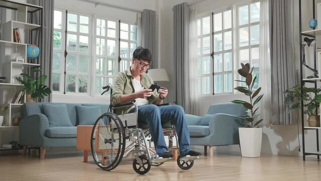Asian Man Sitting In A Wheelchair While Use Mobile Phone And Credit Card Shopping Online At Home
