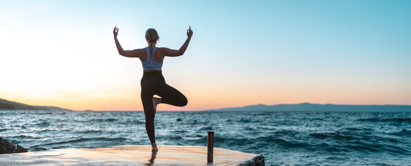 junge attraktive Frau praktiziert Yoga am Meer und macht die Baum Figur