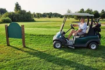 Golfer with prosthetic leg driving golf cart on grass course near golf club nameplate on a sunny...