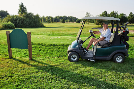 Golfer with prosthetic leg driving golf cart on grass course near golf club nameplate on a sunny day over landscape background and fairway