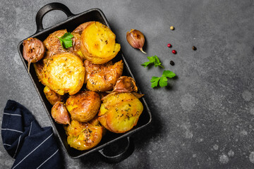 Garlic herbs roast potatoes in cast iron skillet on dark background. Top view, copy space.