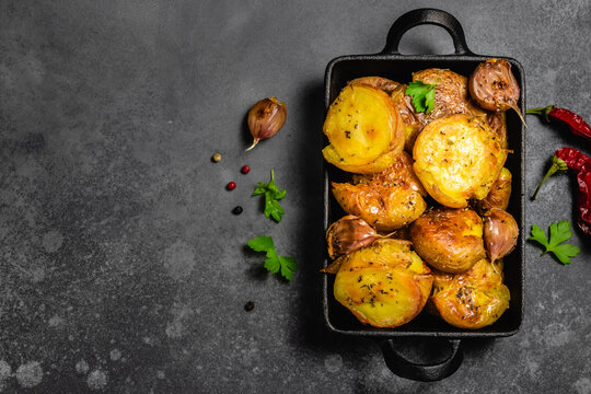 Garlic butter smashed oven baked roast potatoes in cast iron skillet on dark background. Top view, copy space.