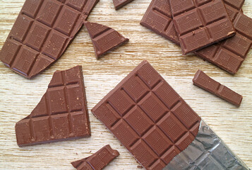 Heap of cracked chocolate bar scattered on wooden background