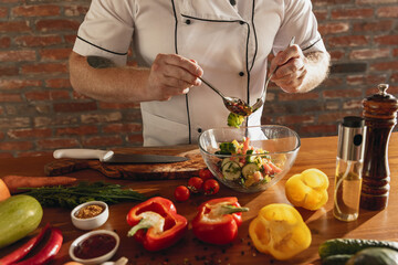 Close-up hands of male chef, cook preparing fresh vegetable salad in his cafe, restaurant kitchen. Concept of a correct, healthy diet.