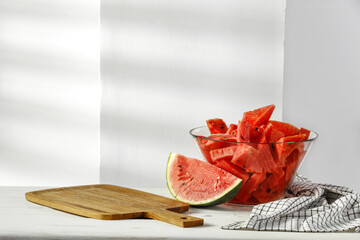 Fresh tasty watermelon on desk and white wall with shadows. 