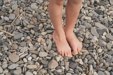 Prevention of flat feet in children. The child walks on the stones with his bare feet. Treatment of valgus foot in children and adults. Close-up of the child's foot on the rocks