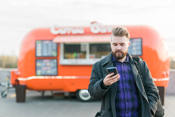 Portrait of handsome young man with smartphone standing in front of food truck