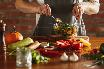 Close-up hands of male chef, cook preparing fresh vegetable salad in his cafe, restaurant kitchen....