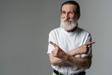 European senior man pointing fingers at opposite sides and smiling