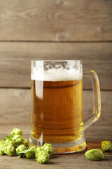 Glass of fresh beer with green hops on a grey background. Vertical photo