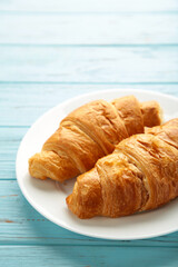 Freshly croissant on plate on blue wooden background. Vertical photo