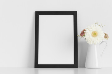 Black frame mockup with a bouquet of flowers on the white table.