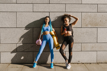Fototapeta na wymiar Black two sportswomen standing together by concrete wall