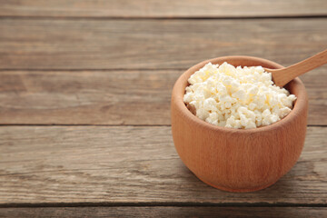 Cottage cheese for breakfast in wooden bowl on brown background.