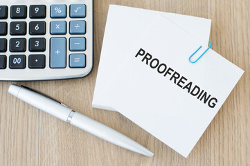 proofreading inscription on a white note card on the table next to a pen and a calculator