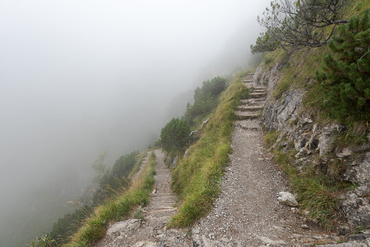 Steep hiking path in the alps on cold autumn day with mist and fog
