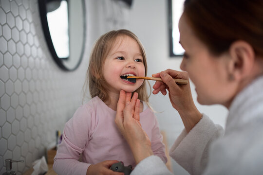 Mother with small daughter brushing teeth indoors in bathroom in the evening or morning.