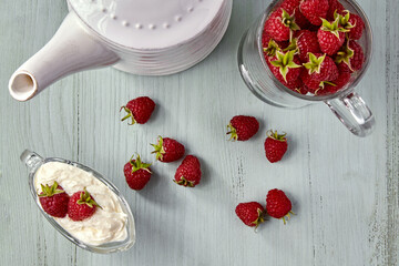 Red raspberries in a glass bowl with cream and in a cup are scattered