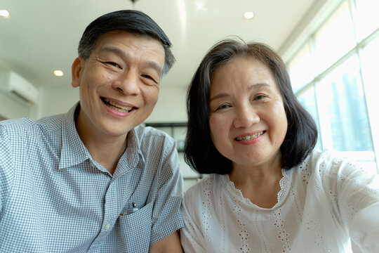 Happy Elderly Asian Couple Doing Facetime Video Calling With A Smartphone At Home Using The Zoom App, Online Meetings, Social Media, New Normal Concepts