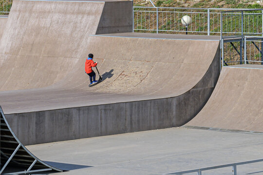 A boy rides a scooter at a skateboarding stadium