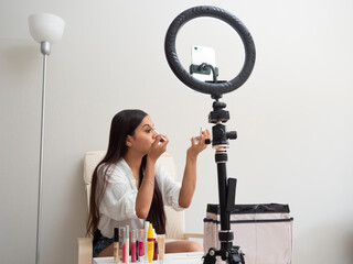 Young Latina content creator girl doing a makeup blog with different feminine products on a chair with a white table and a carpet