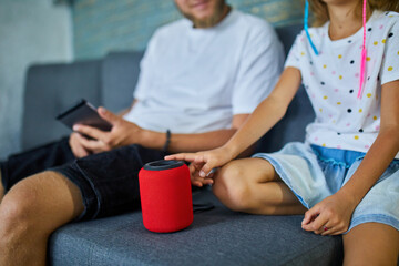 Father and daughter testing talking smart wireless speaker, controlling home devices with a voice commands, sitting on sofa at home, Concept of smart home