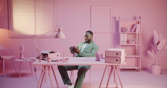 Office worker is procrastinating, smiling and enjoying smartphone phone game app work or message news network. Monochrome pink pastel design room studio monocolor creative with monochrome rose