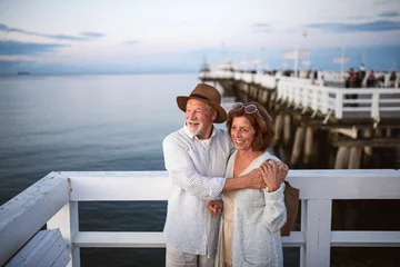 Tuinposter High angle view of happy senior couple hugging outdoors on pier by sea, looking at view. © Halfpoint