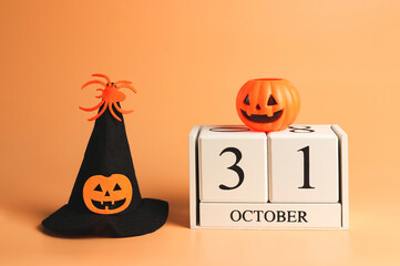 wooden calendar 31 October  with halloween pumpkin on it and Halloween witch hat decorated with pumpkin head and spider  on orange background. Halloween costume concept.