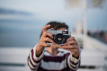 Close up of girl taking photo with camera on pier by sea at sunset, holiday concept.