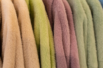 A row of women's faux fur coats low pile on hangers in the store. Bright colors of women's outerwear for the autumn winter season. Close-up of fabric pile texture