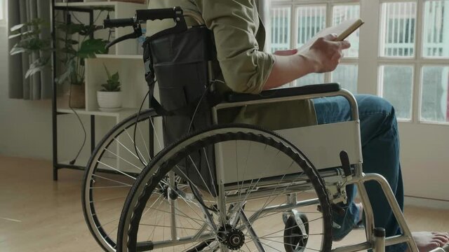 Asian Man Sitting In A Wheelchair Reading Book Near Door In The House
