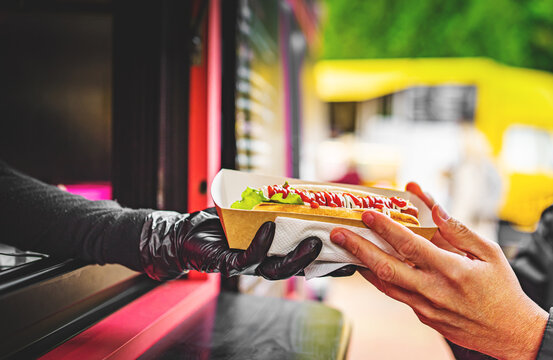 chef hands gives a hot dog to man from food truck on street