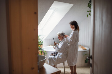 Happy senior mother in bathrobe with adult daughter indoors at home, selfcare concept.