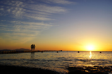 Fototapeta na wymiar Colorful sunset by the ocean, two people walk across the bridge, two silhouettes 