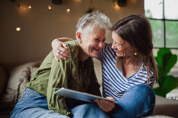 Portrait of happy senior mother with adult daughter indoors at home, using tablet.