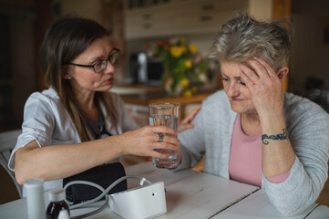 Healthcare worker or caregiver visiting senior woman indoors at home, explaining.