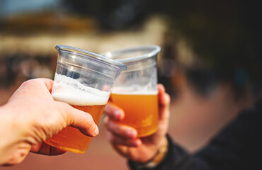 two plastick glass of beer in hand. Beer clinking outdoor