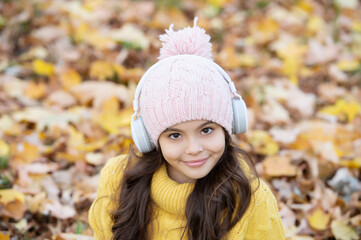 cheerful kid in hat listening music in headphones outdoor in park, autumn