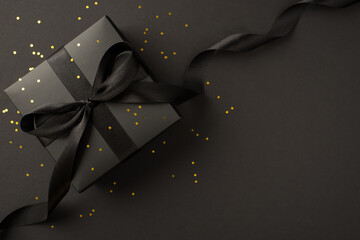 Top view photo of giftbox in black packaging with black ribbon bow and golden sequins on isolated...