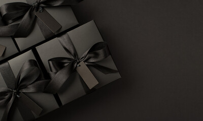 Top view photo of black gift boxes with tags and black ribbon bow on isolated black background with copyspace