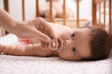 Mother giving pacifier to her cute little baby in crib at home, closeup