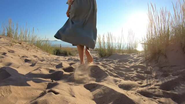 Close-up of the slender legs of a young woman walking along a deserted northern beach among the sand dunes in the rays of the setting rising sun. Yyteri beach, Finland